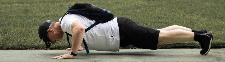 Colby Warren, a manager on CAPTRUST's marketing team, does a pushup on a concrete sidewalk wearing his rucking backpack